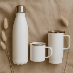 Styled shot of a white stainless steel water bottle, travel mug, and enamel mug on neutral fabric with soft light — showcasing premium reusable drinkware for intentional, low-waste living.